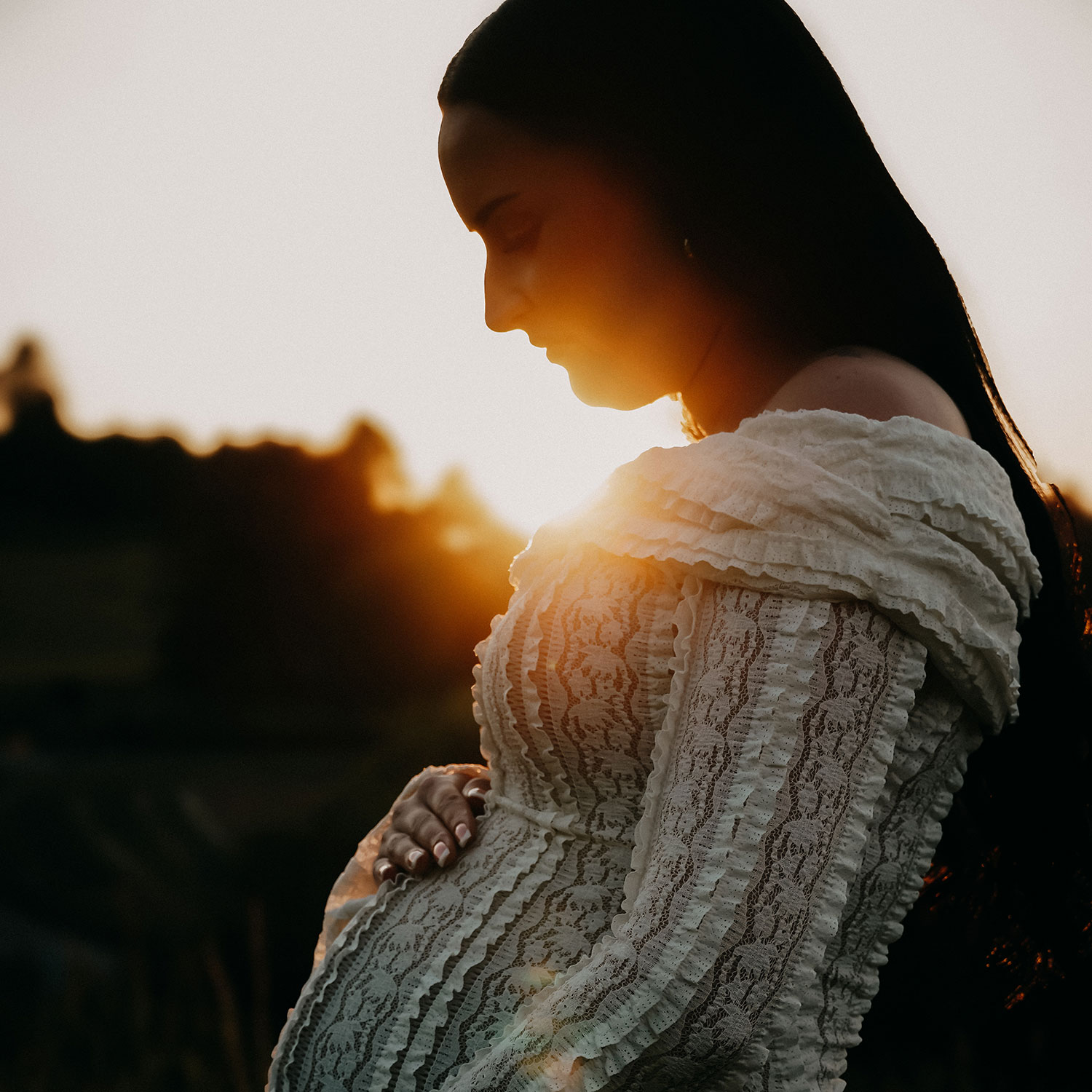 Eine Frau schaut im Sonnenuntergang auf ihren Babybauch 
